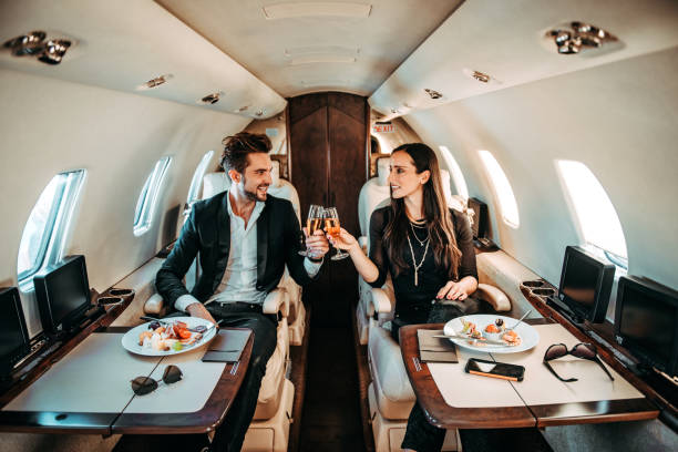 Successful couple making a toast with champagne glasses while having canapes aboard a private airplane Rich couple making a toast with champagne glasses while eating canapes aboard a private jet. first class photos stock pictures, royalty-free photos & images