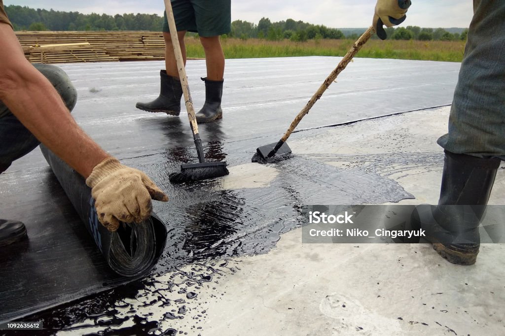 Roofer worker painting bitumen praimer at concrete surface by the roller brush Waterproofing Roofer worker painting bitumen praimer at concrete surface by the roller brush Waterproofing 2018 Rooftop Stock Photo