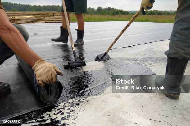 Roofer Worker Painting Bitumen Praimer At Concrete Surface By The Roller Brush Waterproofing Stock Photo - Download Image Now