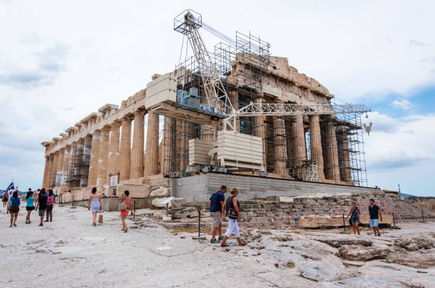 Athens, Greece - June 12, 2013: The famous Parthenon on Acropolis hill under reconstruction surrounded by scaffolding and standing construction crane in the front of the temple with walking tourists