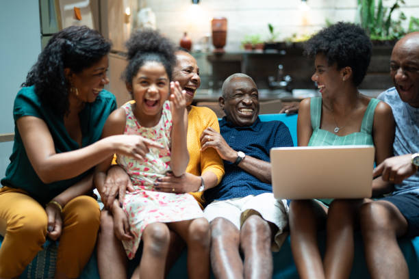 afrikanische hispanische familie zusammen zu hause während einer von ihnen benutze laptop --mehrgenerationen familie - family domestic life senior adult computer stock-fotos und bilder