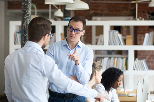 Middle aged angry mentor, coach blaming furious subordinates, boss criticize work of man intern, trainee in office, worker justifying, discussing with supervisor, businesspeople arguing