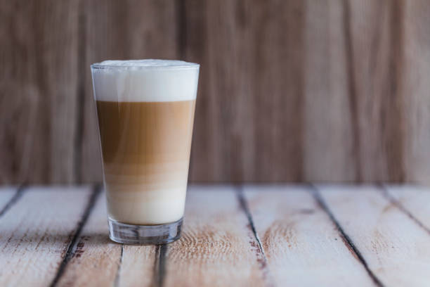 Caffe latte macchiato coffee layered with milk Caffe latte macchiato coffee layered with milk in a high drinking glass. There drink is on a wooden table with the background wooden as well. Empty space to the right. latte stock pictures, royalty-free photos & images