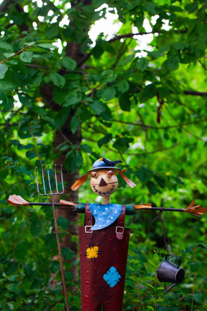 A person dressed as a scarecrow with a burlap mask, straw hat, and plaid shirt emerges from a stone well at night, raising arms with straw.