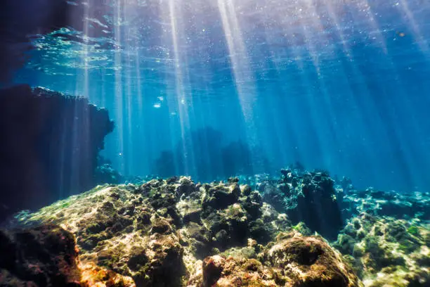 The scene from underneath the Andaman Sea.  The location is the famous destination Ko Haa Island 3, Krabi province, Thailand.  Stunning limestone Karst Islands rise up from the Andaman Sea.  Famed for their stunning coral reefs.  A popular site with Scuba Divers and Snorkelers.  Here we see the morning sunbeams piercing the blue sea onto the coral reef.  An ideal background image.  Sony mirrorless camera used in underwater housing.