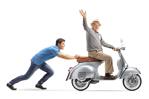 Full length shot of a young guy pushing a senior on a vintage scooter who is waving isolated on white background