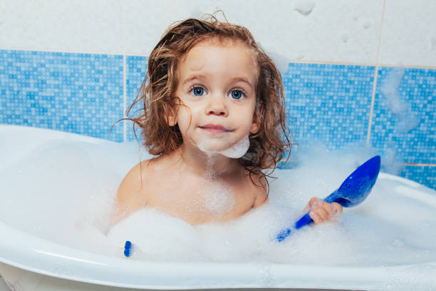 Fun cheerful happy toddler baby taking a bath playing with foam bubbles. Little child in a bathtub. Smiling kid in bathroom on blue background. Hygiene and health care. Fun cheerful happy toddler baby taking a bath playing with foam bubbles. Little child in a bathtub. Smiling kid in bathroom on blue background. Hygiene and health care girls bath stock pictures, royalty-free photos & images