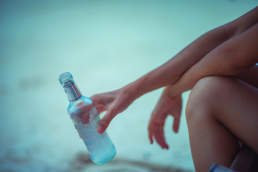 bottle of liquid light beer in hand of young woman, feel comfortable and relax sitting on deck chair beach, happy enjoy with  drink alone