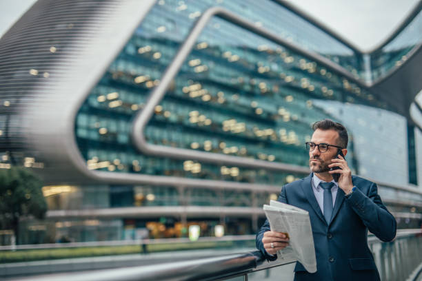 istock Man in suit reading newspaper and talking on mobile 1092679332
