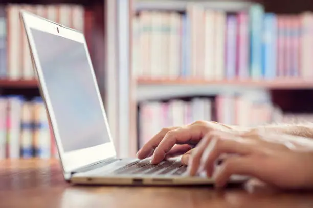 Hands typing on laptop computer in library concept for education, writer or research