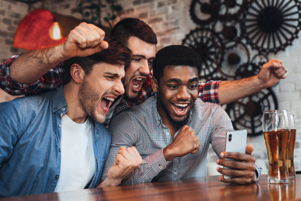 Men watching football on smartphone in bar Men watching football on smartphone and drinking beer in bar online games to play with friends stock pictures, royalty-free photos & images
