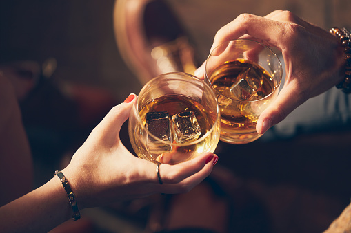 A couple makes a toast with two glasses of whiskey