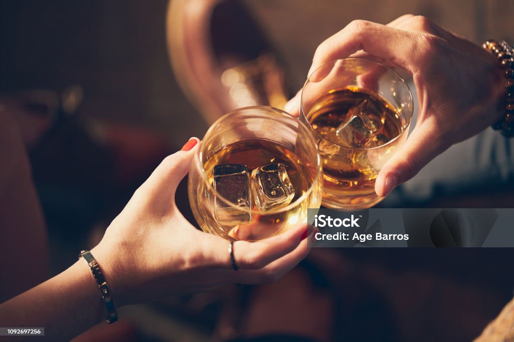 A couple makes a toast with two glasses of whiskey Celebratory Toast Stock Photo