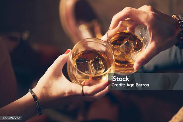 A Couple Makes A Toast With Two Glasses Of Whiskey Stock Photo - Download Image Now - Celebratory Toast, Alcohol - Drink, Bourbon Whiskey