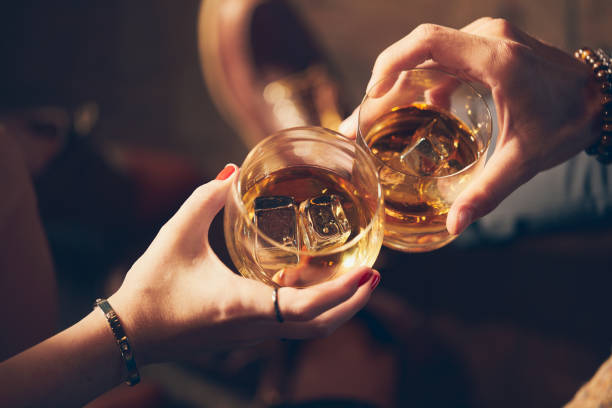 a couple makes a toast with two glasses of whiskey - toasted imagens e fotografias de stock