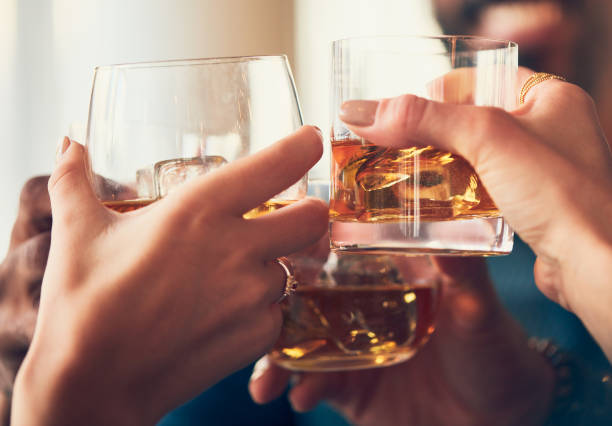 группа друзей делает тост с человеком на размытом фоне - whisky alcohol glass party стоковые фото и изображения