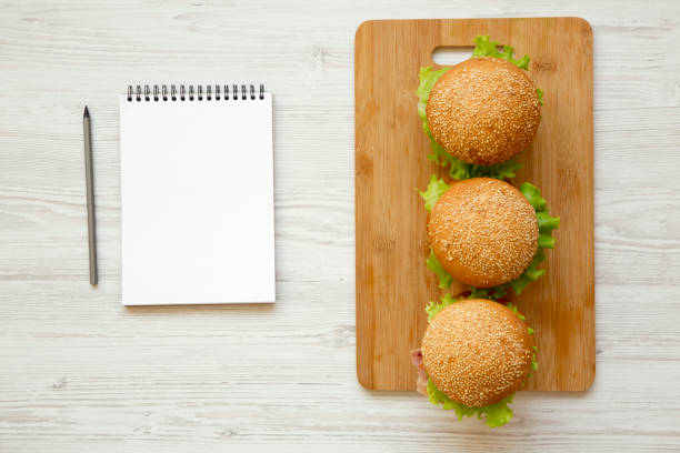 Cheeseburgers and blank notepad on white wooden background, overhead view. Flat lay, from above. Space for text.