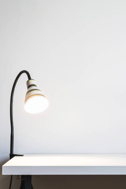 istock Luminous table lamp on a white desk. White wall for mock up or copy space 1092699740