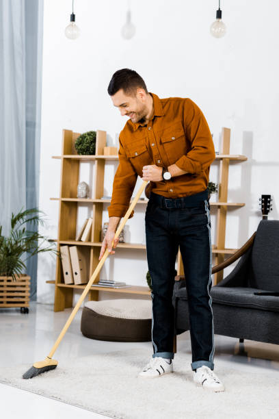 istock handsome man cleaning carpet with broom in modern living room 1092701962