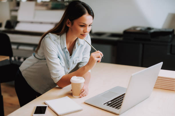 istock Attractive young lady with hot drink looking at laptop 1092702684
