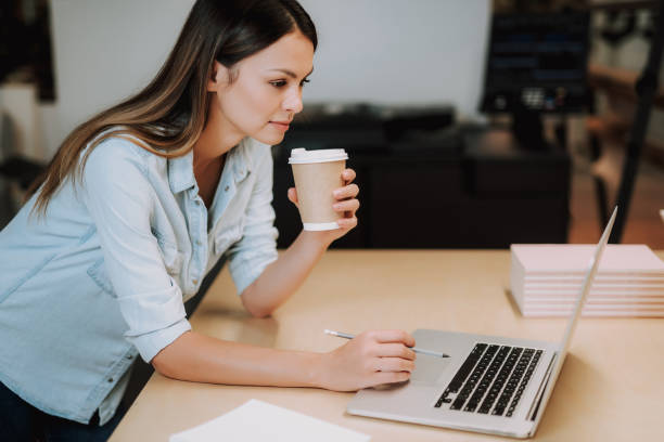 istock Beautiful young lady with hot drink looking at laptop 1092702694