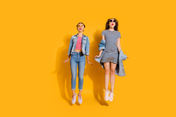 istock Full legs length body size two funny funky glad positive grinning cheerful charming friendly optimist lady in glasses spectacles casual denim jeans outfit jump isolated on yellow bright background 1092709364