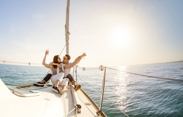 jeune couple amoureux sur voilier avec champagne à rétro-éclairage doux coucher de soleil - mode de vie des gens heureux sur la notion de luxe exclusif - se concentrer sur filtre soleil après-midi chaud - distorsion de l’objectif fisheye - sailboat sunset sailing nautical vessel photos et images de collection