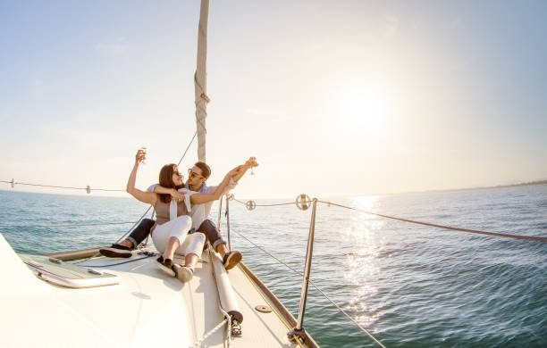 young couple in love on sail boat with champagne at sunset - happy people lifestyle on exclusive luxury concept  - soft backlight focus on warm afternoon sunshine filter - fisheye lens distortion - sailboat sunset sailing nautical vessel imagens e fotografias de stock
