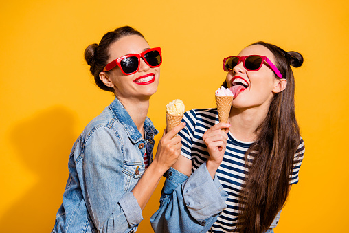 Two brunette hair lady isolated on yellow vivid background in glasses spectacles make beaming white toothy smile eating sugar tasty appetiser snack