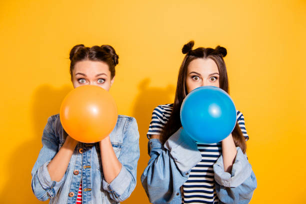 leisure lifestyle concept. close up portrait of two beautiful attractive adorable brunette hair lady look at camera stand isolated on yellow bright background blow fly ball - hair bun hairstyle beautiful looking imagens e fotografias de stock