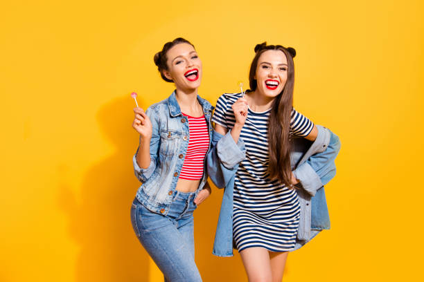 istock Two grinning cheerful charming friendly optimist brunette hair lady look at camera stand isolated on yellow vivid background hold sugar sweet yummy caramel confectionery dessert in hands 1092715584