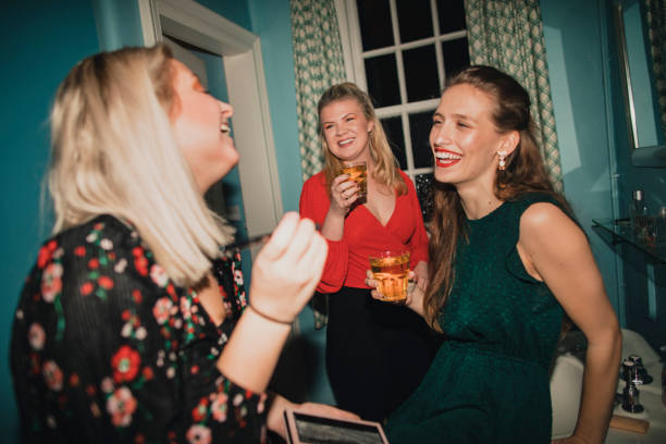 Girls Getting Ready in the Bathroom Three young women are applying makeup with a drink in the bathroom at a house party. ladies night stock pictures, royalty-free photos & images