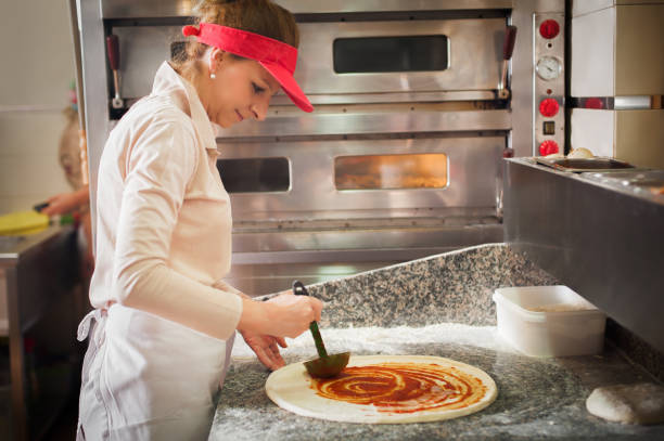 cook spreading tomato sauce over pizza dough - wheat pasta flour italy imagens e fotografias de stock