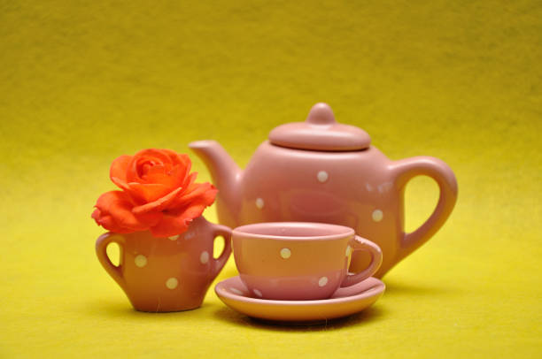 A teacup and a kettle with an orange rose on a yellow background