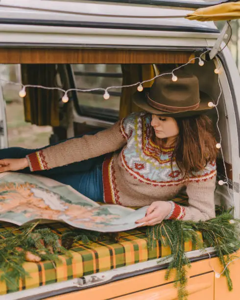 Young Caucasian woman in hat  reading map laying in old camper van