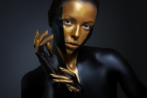 Beautiful girl with gold and black paint on her face and body. Female portrait with creative makeup. The particles of the metal powder for gold paint