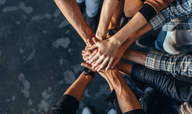 Symbol of teamwork, cooperation and unity Top view of creative professionals putting their hands together as a symbol of teamwork, cooperation and unity. Stack of hands of men and woman. team cooperation stock pictures, royalty-free photos & images