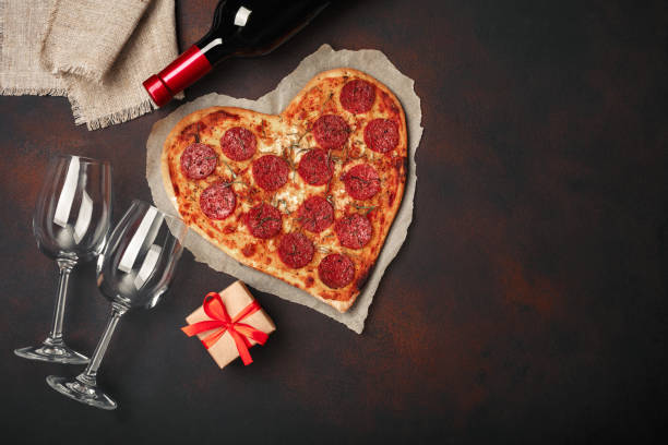 istock Heart shaped pizza with mozzarella, sausagered, wine bottle, two wineglass, gift box on rusty background 1092746070