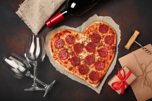 istock Heart shaped pizza with mozzarella, sausagered, wine bottle, two wineglass, gift box on rusty background 1092746194