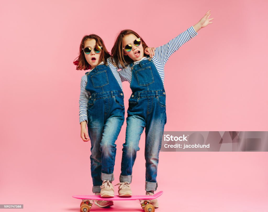 Stylish cute girls with skateboard Stylish cute girls with skateboard and wearing fashion clothes on pink background. Happy children with skateboard enjoying together. Child Stock Photo