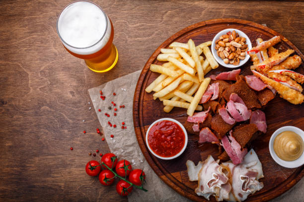 Big set of snacks for beer or alcohol and it includes smoked pork meat, french fries, fried bread, crab sticks and nuts Big set of snacks for beer or alcohol and it includes smoked pork meat, french fries, fried bread, crab sticks and nuts served with sauces on a wooden background. Top view. pub table top view stock pictures, royalty-free photos & images