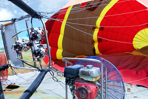 A large gas burner and a large industrial gasoline fan inflate a balloon, a close-up shot.