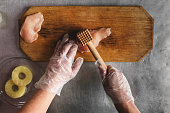 cook prepares chicken on a wooden cutting board, hands, chicken, pineapple, gloves. meat tenderizer. recipe for chicken fillet with cheese and pineapple. top view on kitchen table