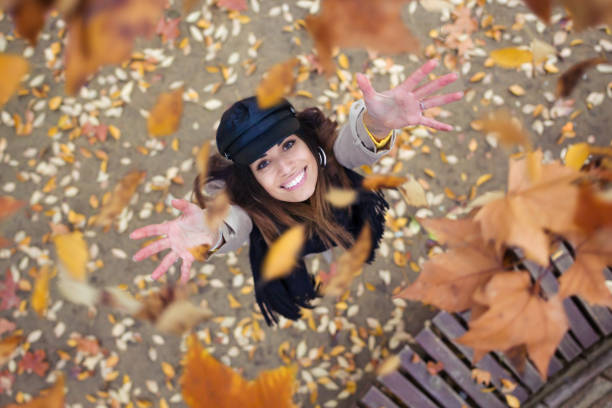 かなり若い女性の腕秋の公園には、木から葉が落ちるように調達して空を見上げします。 - autumn women smiling leaf ストックフォトと画像