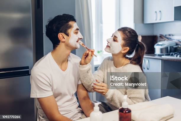 Woman Applying Clay Mask On Her Boyfriends Face Young Loving Couple Taking Care Of Skin At Home Stock Photo - Download Image Now