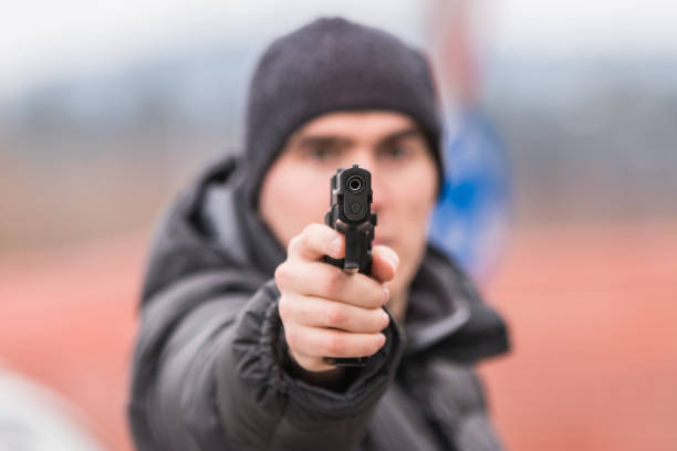 un uomo che punta una pistola contro l'obiettivo - gun gunman handgun men foto e immagini stock