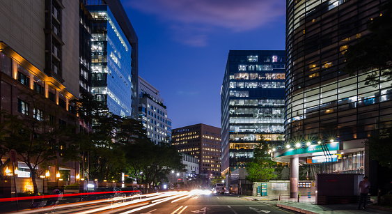 Street of Seoul, South Korea business district with lights shining in windows. Light trail of passing car is visible in foreground. Photo is taken during beautiful summer night.