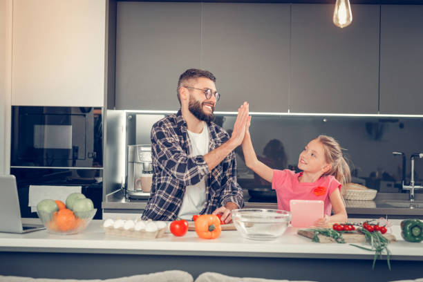 istock Tall bearded dark-haired man in a checkered shirt making breakfast with his daughter 1092779770