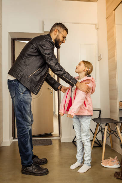 istock Handsome dark-haired bearded man in eyewear putting a coat on his daughter 1092779998