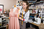 Serious woman professional measuring dress at  mannequin at  workshop